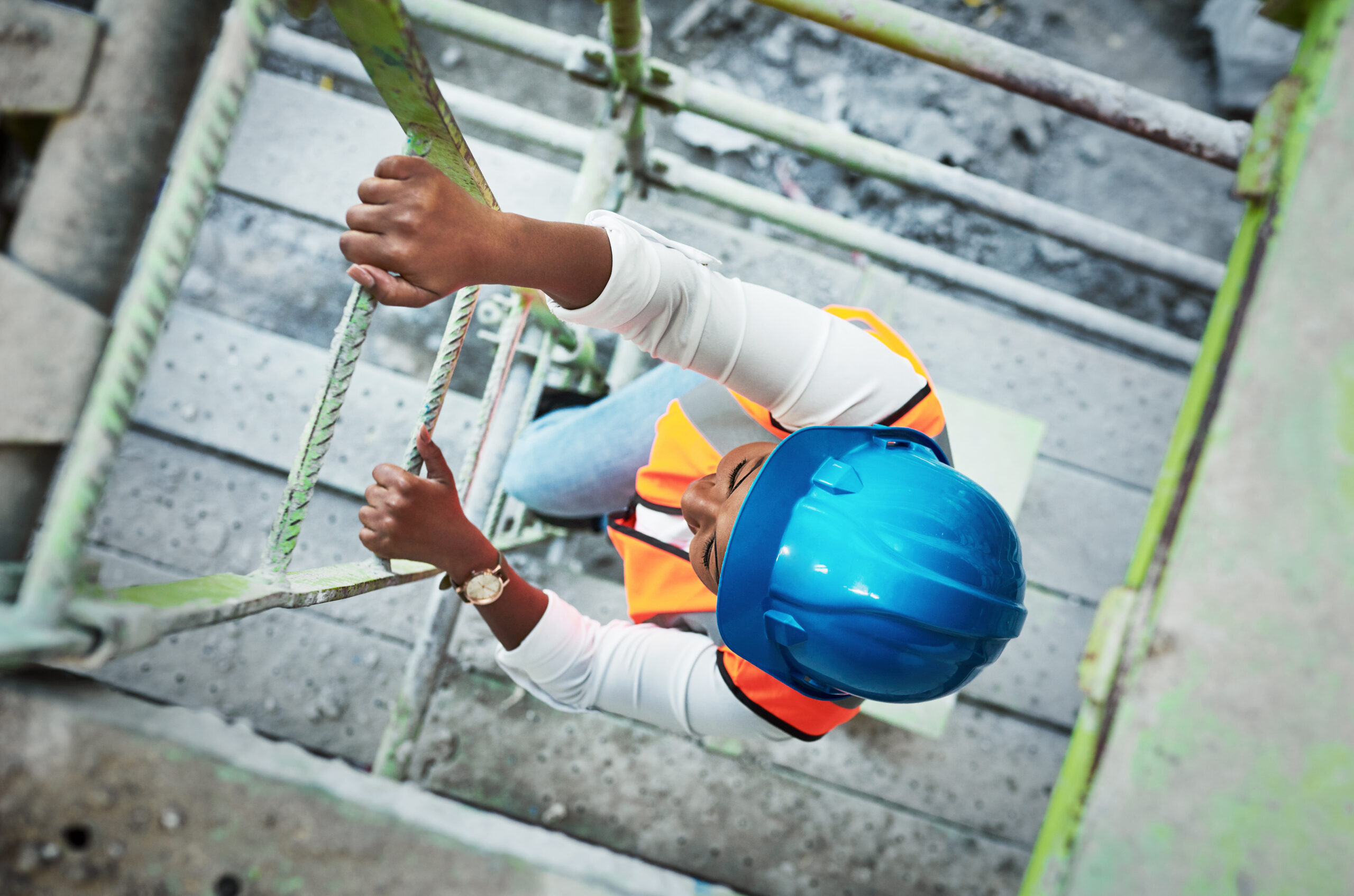 Shot of a young woman climbing up a ladder at a construction site.