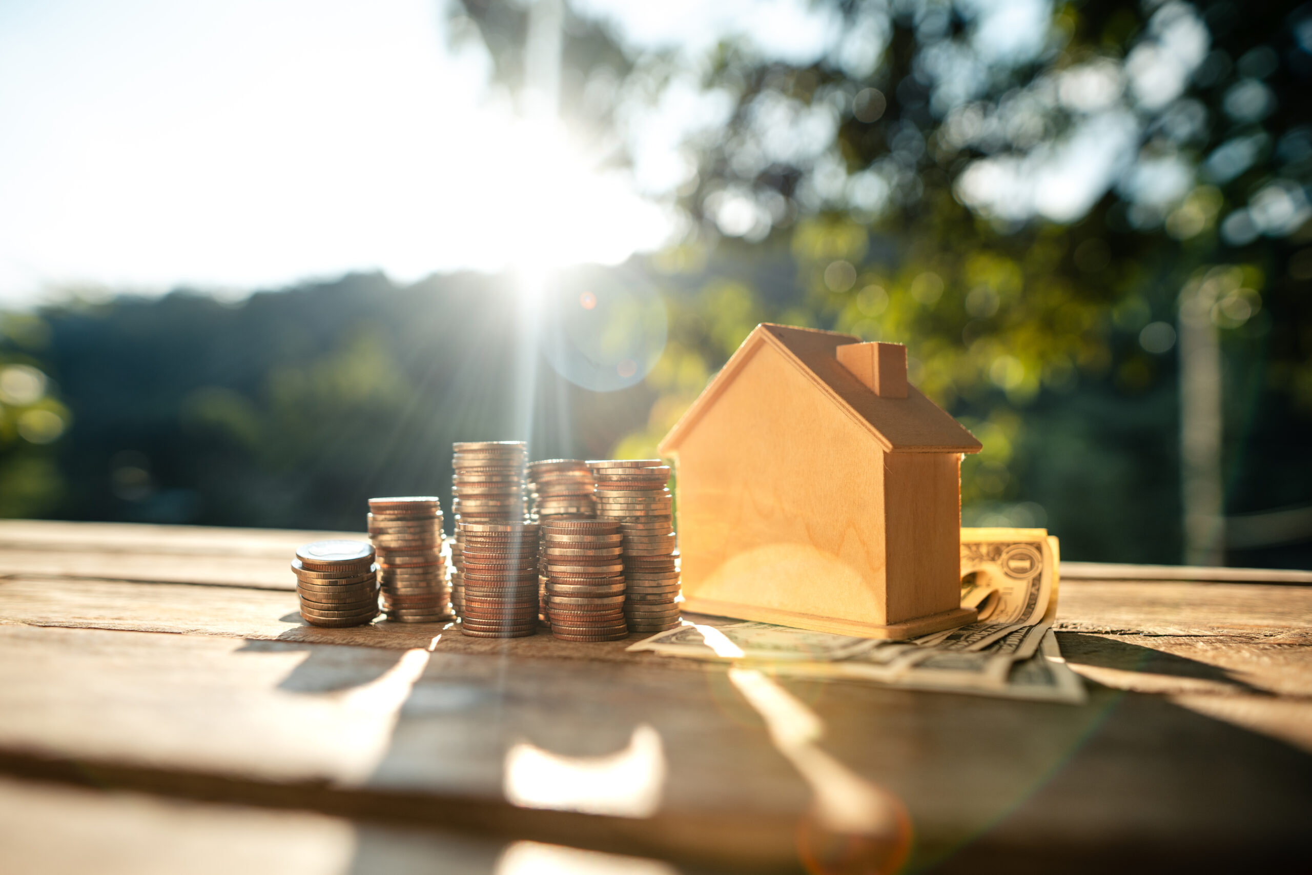 Stacked money and house savings on wooden table, natural background light